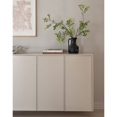 a vase with some green plants on top of it next to a wall mounted art piece