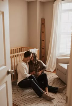 a man and woman sitting on the floor in front of a crib