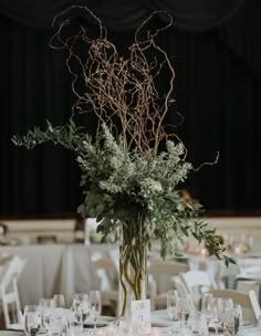 a vase filled with lots of greenery sitting on top of a table covered in glasses