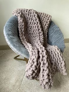 a large chunky knitted blanket sitting on top of a blue chair next to a white wall