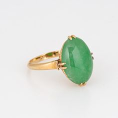 This is part of Chairish’s Fine Jewelry assortment.  Stylish vintage jade ring (circa 1950s to 1960s) crafted in 14 karat yellow gold.   Jade measures 14mm x 9.5mm. The jade is in good condition and free of cracks or chips.   The oval mount highlights beautiful green jade. Measuring just over 1/2 inch in length the ring makes a nice statement on the hand. The low rise ring (7mm - 0.27 inches) sits comfortably on the finger.    The ring is in good condition and was lightly cleaned and polished. Vintage Jade Ring, Heirloom Yellow Gold Jade Rings, Classic Green Jade Rings, Imperial Jade Ring, Vintage Jade Cabochon Ring, Vintage Jade Jewelry Hand-strung, Green Cocktail, Yellow Gold Cocktail Ring, Gold Cocktail