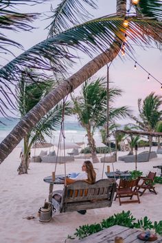 a woman is sitting on a swing at the beach