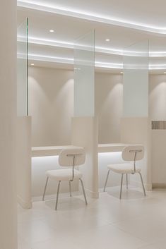 two white chairs in a room with mirrors on the wall and lights on the ceiling