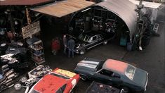 an overhead view of several old cars parked in front of a garage with people looking at them