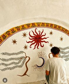 a man sitting on the ground in front of a wall with an artistic design painted on it