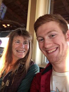 a man and woman smile for the camera while sitting next to each other in front of a window