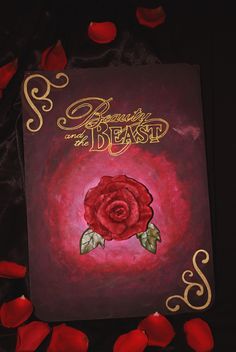 a red rose on top of a purple book with gold lettering that reads beauty and the beast