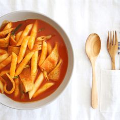 a white bowl filled with pasta and sauce next to a wooden spoon on top of a table