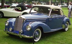 an old blue car parked on top of a lush green field next to other antique cars