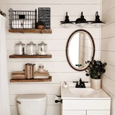 a white toilet sitting next to a sink in a bathroom under a wooden shelf filled with bottles