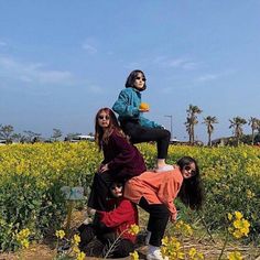 four people are standing in a field with yellow flowers and one person is sitting on top of the other