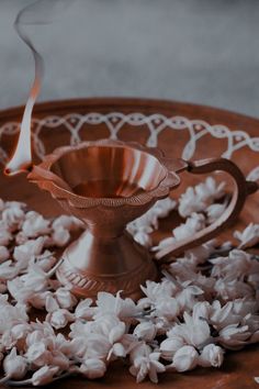 a small metal bowl filled with white flowers on top of a wooden table next to a candle