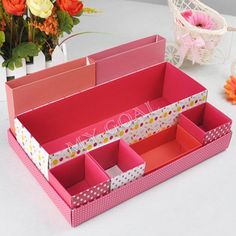 two pink boxes with polka dots on them sitting next to flowers and a basket in the background