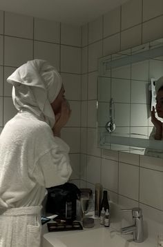 a woman in a bathrobe is looking at her reflection in the bathroom mirror