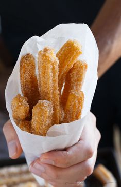 a person holding a paper bag filled with sugar coated doughnuts