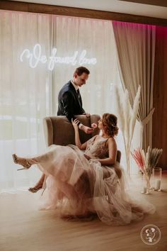 a man and woman sitting on a chair in front of a neon sign that reads we are married