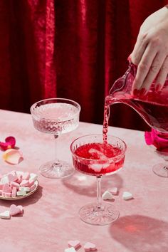 a person pouring pink liquid into a wine glass on a table with marshmallows