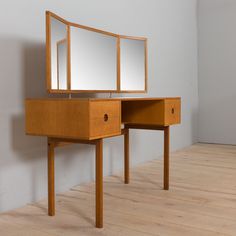 a wooden desk with two mirrors on top of it next to a white wall and wood floor