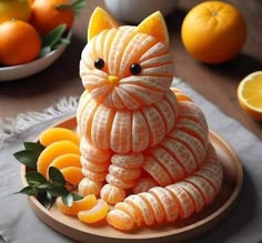 a cat made out of fruit sitting on top of a plate next to oranges