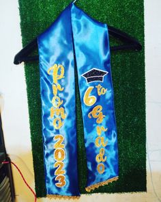 two blue graduation sashes with gold writing on them sitting next to a green wall