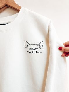 a person holding onto a white sweatshirt with the word pennus on it and a cat's head