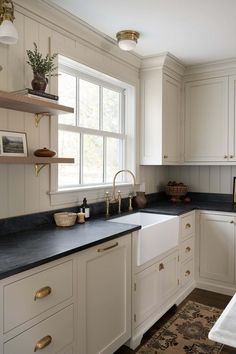 a kitchen with white cabinets and black counter tops, gold pulls on the faucets