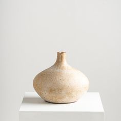 a white vase sitting on top of a white block in front of a gray wall