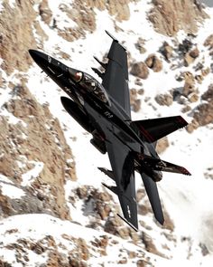 a fighter jet flying through the air over snow covered mountains