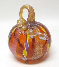 an orange and yellow glass ornament on a white surface with gold trimmings