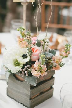 a wooden box filled with flowers on top of a white table cloth covered dining room table