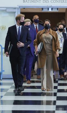 two people wearing face masks walking down a hall with other people in suits and ties