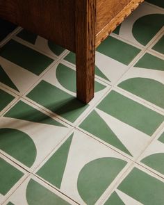 a wooden table sitting on top of a green and white tile covered floor next to a wall