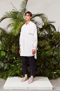 a man standing on top of a white platform in front of green plants and trees