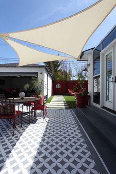 an outdoor patio with table and chairs under a large shade sail over the dining area