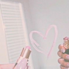 a person holding a lipstick in front of a heart drawn on the wall