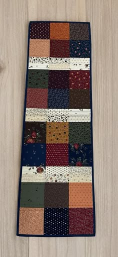 a patchwork table runner made out of various fabrics on a wooden surface with scissors