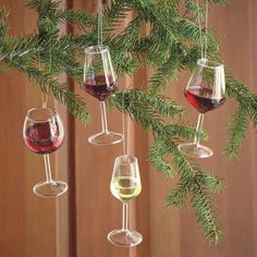 three wine glasses hanging from a christmas tree with pine needles and red wine in them