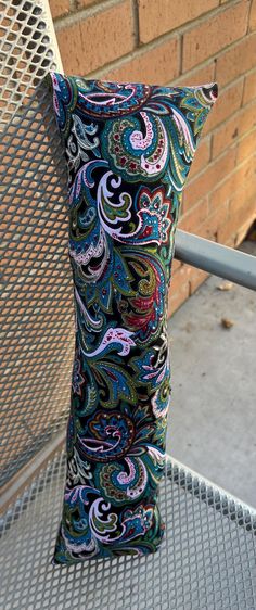 a decorative pillow sitting on top of a metal bench next to a brick wall and fence