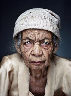 an old woman with blue eyes and a white hat on her head is looking at the camera