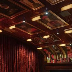 an empty theater with red curtains and pictures on the walls, along with lights hanging from the ceiling