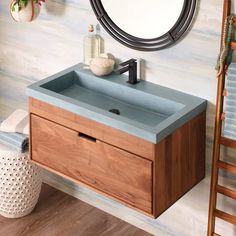 a bathroom vanity with a blue counter top and wooden cabinet under a round mirror on the wall