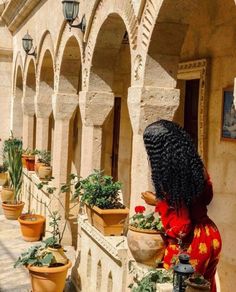 a woman with long black hair standing in front of potted plants on the outside of a building