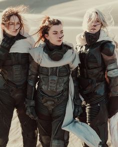 three women dressed in black and white standing next to each other on the sand dunes