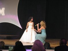 two women on stage with one holding a microphone and the other wearing a white dress