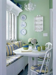 a dining room with green walls and white chairs, plates on the wall and flowers in vases at the table