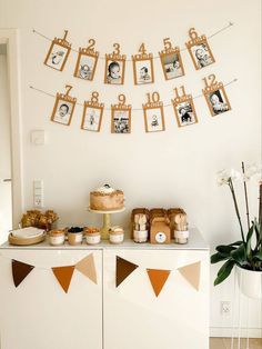 a table topped with cake next to pictures and bunting on the wall above it