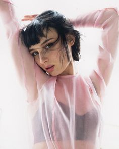 a woman is posing with her arms behind her head and wearing a sheer pink top