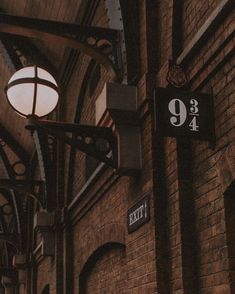 an exit sign hanging from the side of a brick building next to a light fixture