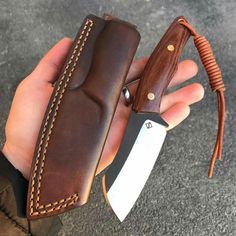 a person holding a knife in their hand with a brown leather sheath on the handle