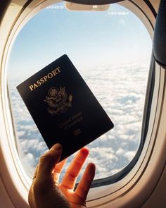 someone holding up a passport in front of an airplane window with the sky and clouds behind them